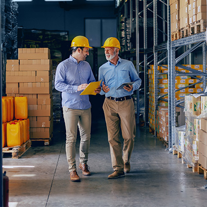 Zwei Geschäftspartner in formeller Kleidung und mit gelben Schutzhelmen gehen spazieren.