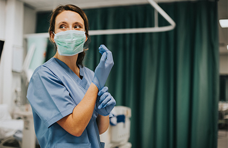 Krankenschwester mit Maske zieht Handschuhe an